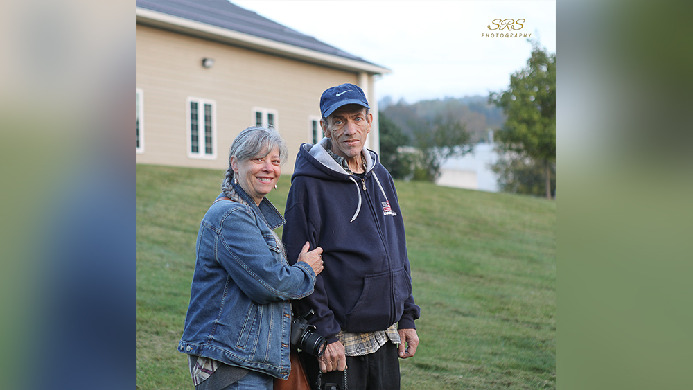 Man and woman smile at camera while standing on grass