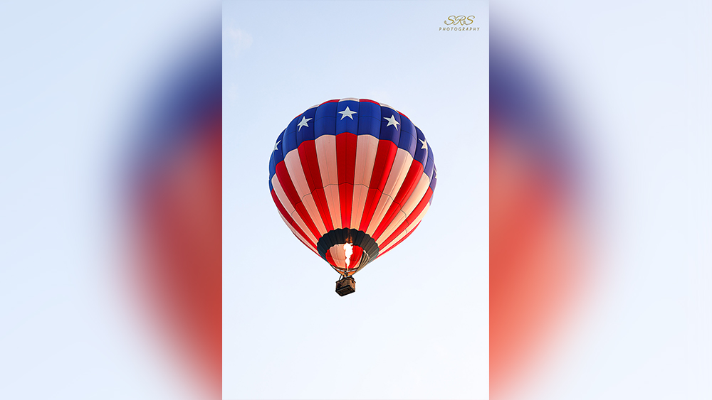Red white and blue hot air balloon rising into clear blue sky