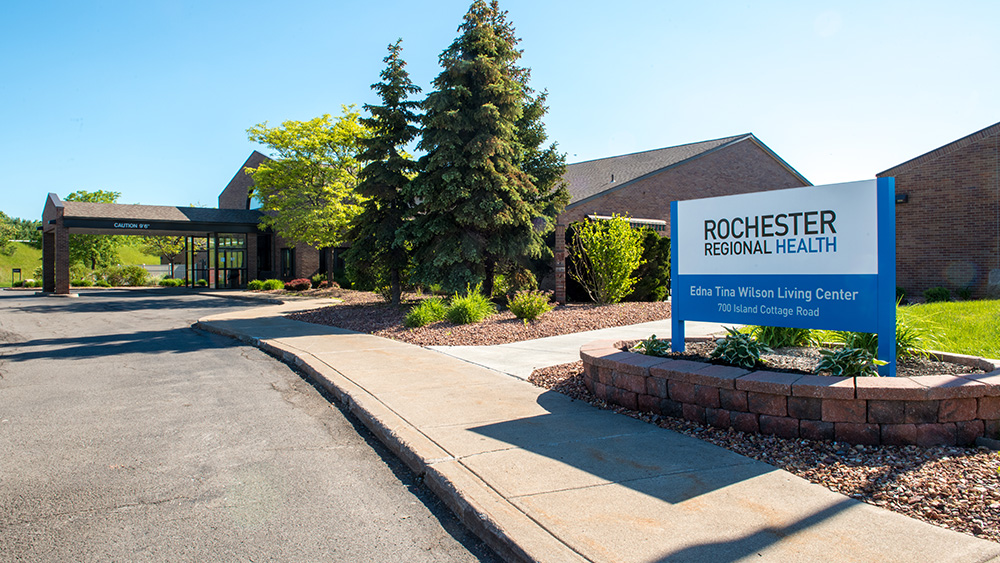 Brick nursing home building with blue sign green pine trees and blue sky