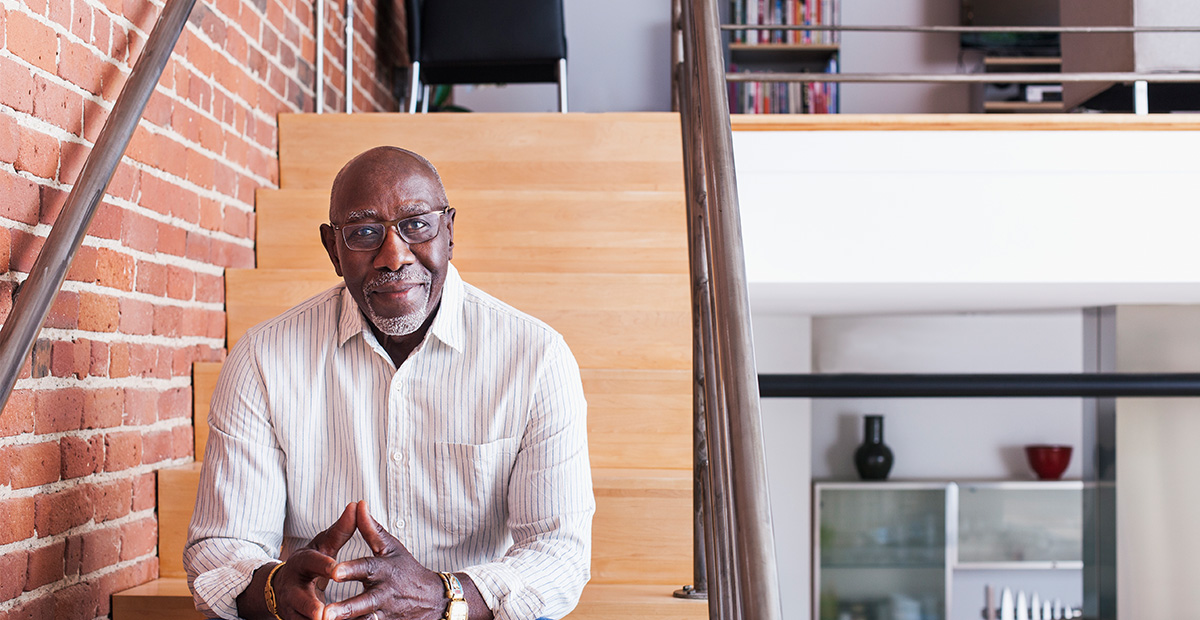 A Black man sitting on wooden stairs in a modern home