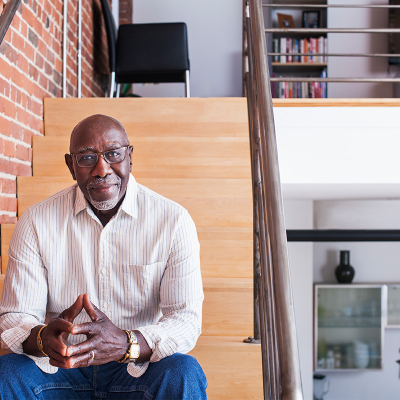 A Black man sitting on wooden stairs in a modern home
