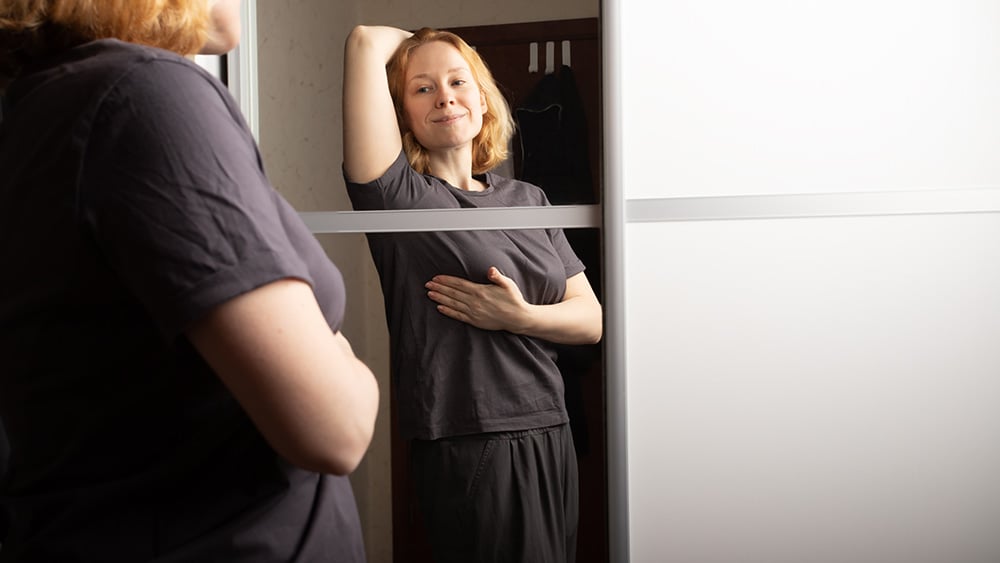 woman doing self breast check in mirror at home