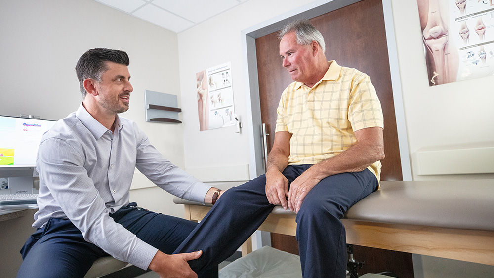 Orthopedic doctor looks at male patient's knee
