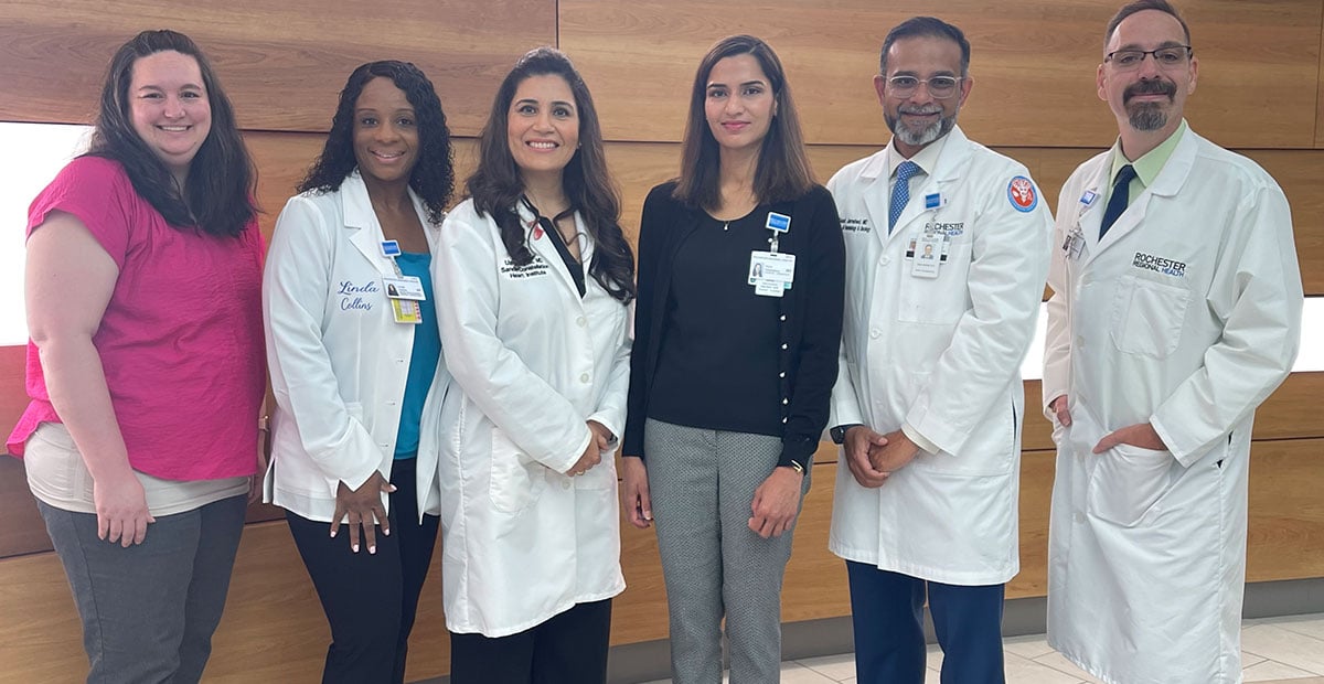 The Cardiology-Oncology team at Sands-Constellation Heart Institute gathered in front of a wood panel background