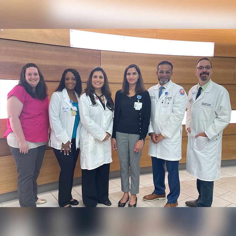 The Cardiology-Oncology team at Sands-Constellation Heart Institute gathered in front of a wood panel background