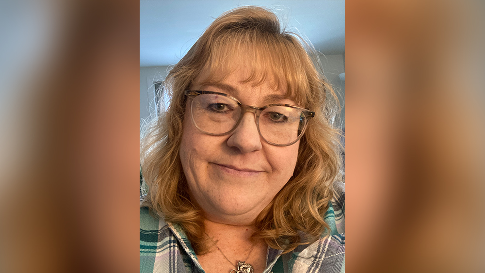 white middle aged woman with auburn hair and glasses smiling in selfie photo