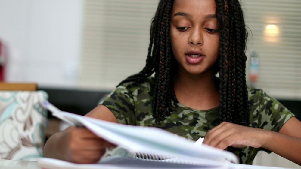 Black teen girl doing homework at home writing paper studying