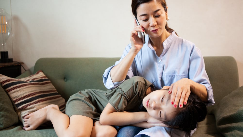 mother on phone while sick child lies on her lap