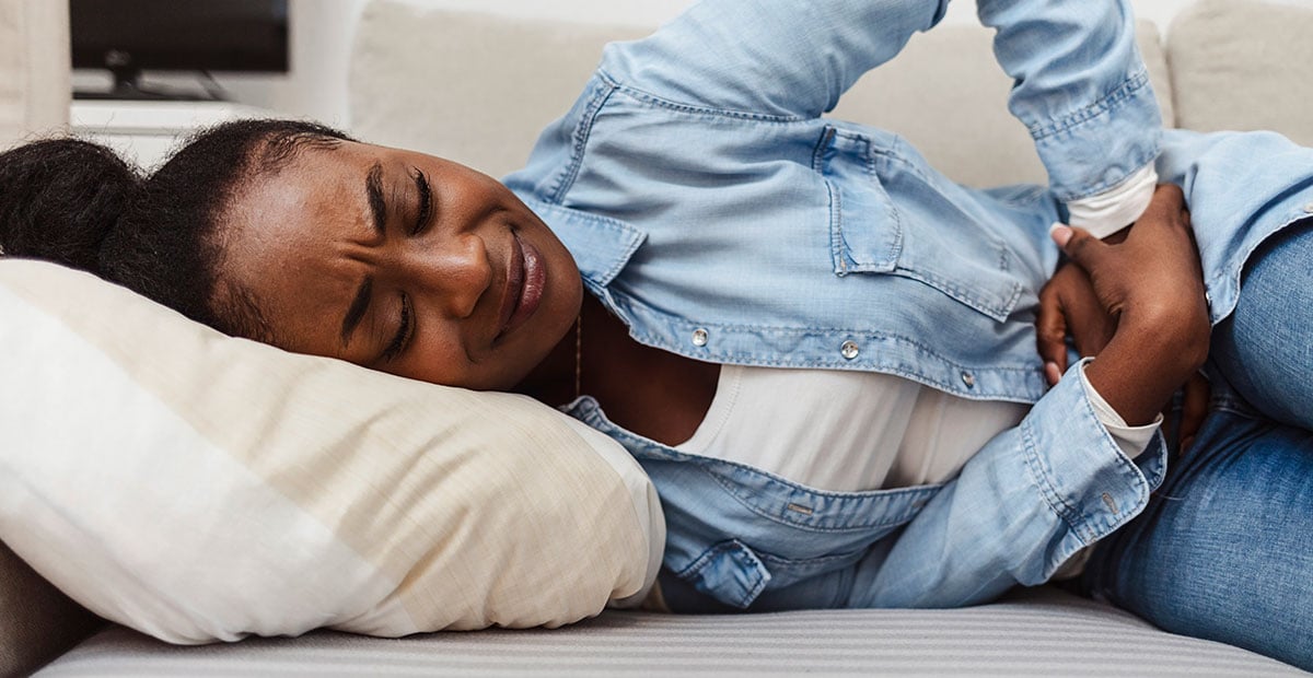 Woman in painful expression holding hands against belly