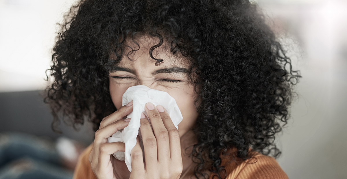 Shot of a young woman blowing her nose with a tissue at home