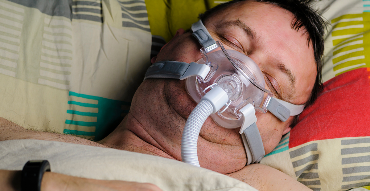 Middle aged overweight man wears a CPAP to help him sleep due to sleep apnea