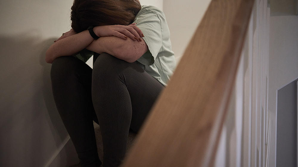 White woman sitting in stairwell with head down in arms