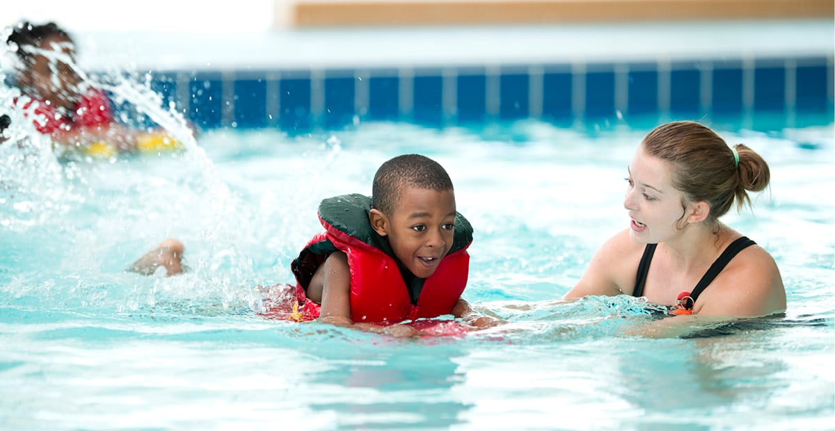 A boy swimming in a pool with a life jacket