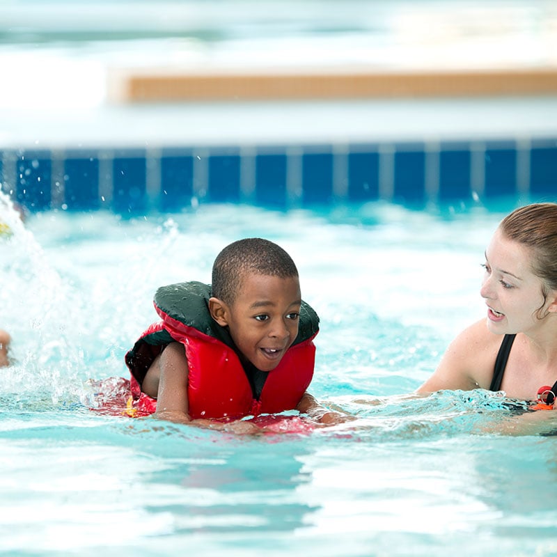 A boy swimming in a pool with a life jacket