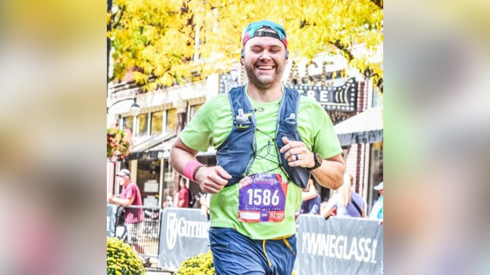 White man in green shirt hydration vest smiling at camera during marathon race