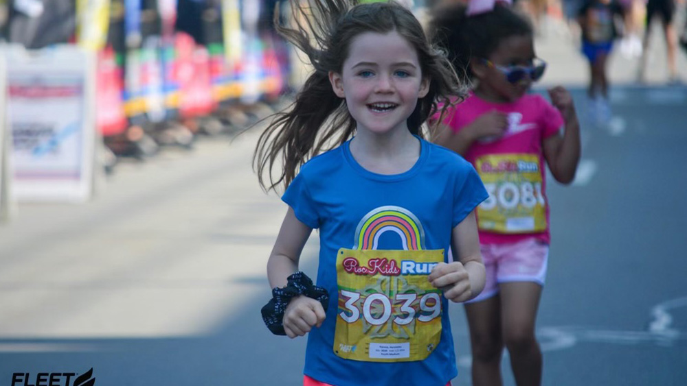 Young white girl in blue shirt smiling at camera while running