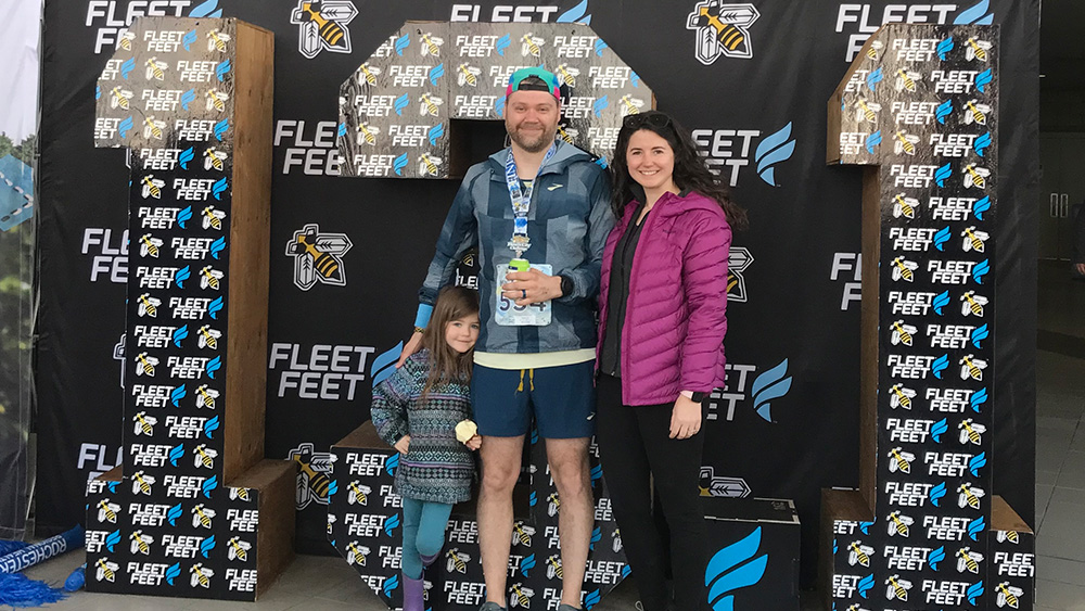 Young girl middle aged man middle aged woman in running gear stand in front of 13.1 sign smiling