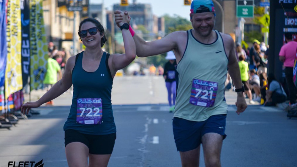 Wife and husband cross finish line smiling running race while holding hands