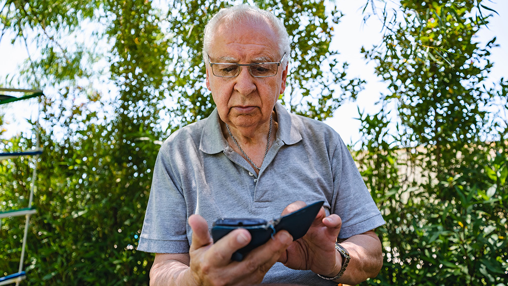 Senior Latin man is sitting in the yard and typing a message on smart phone