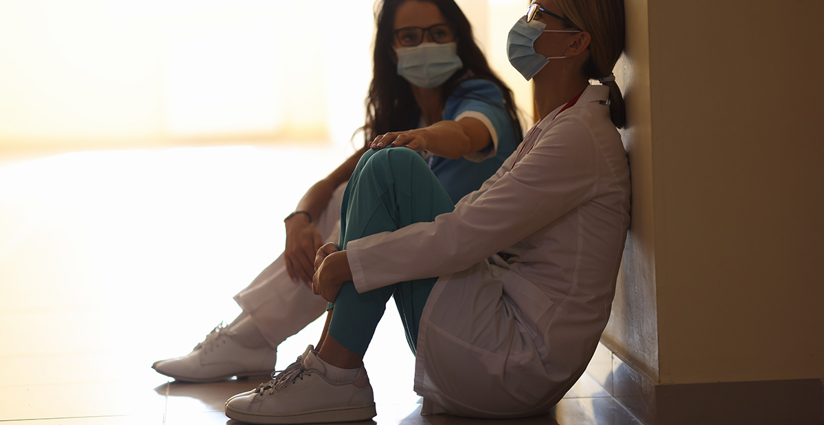 Tired women doctors are sitting in masks in corridor