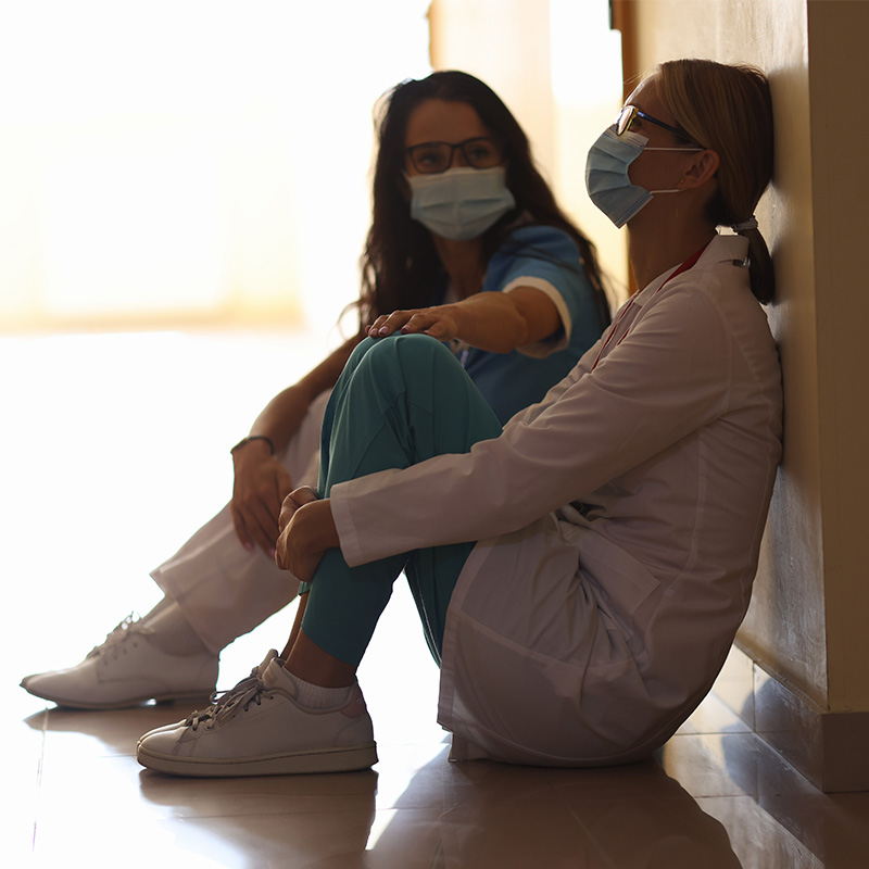 Tired women doctors are sitting in masks in corridor
