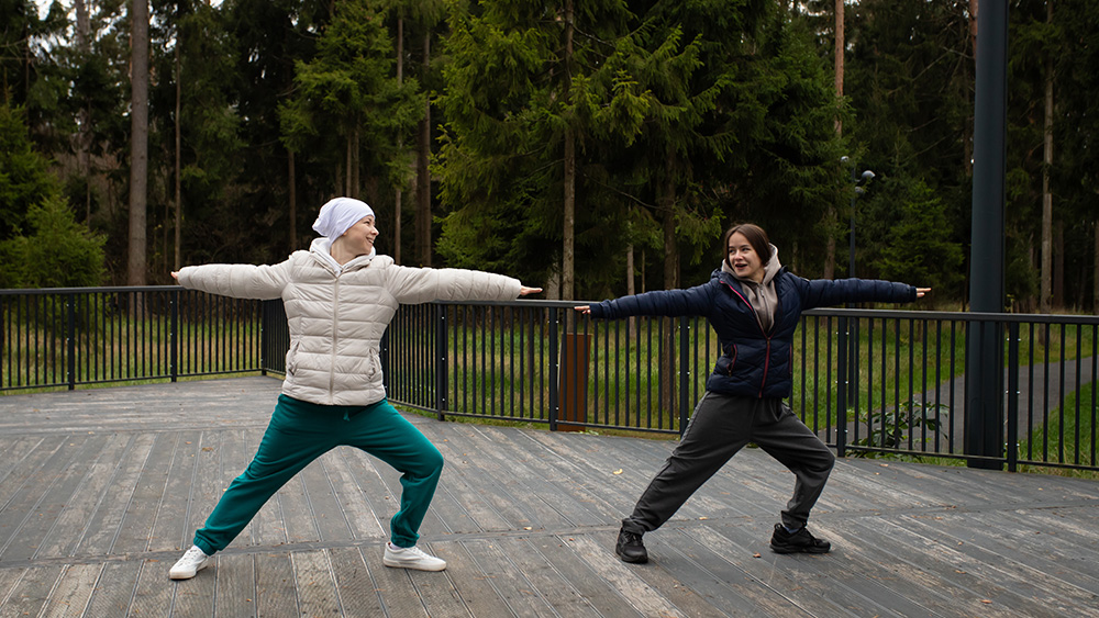 Female cancer patient and woman doing yoga outdoors