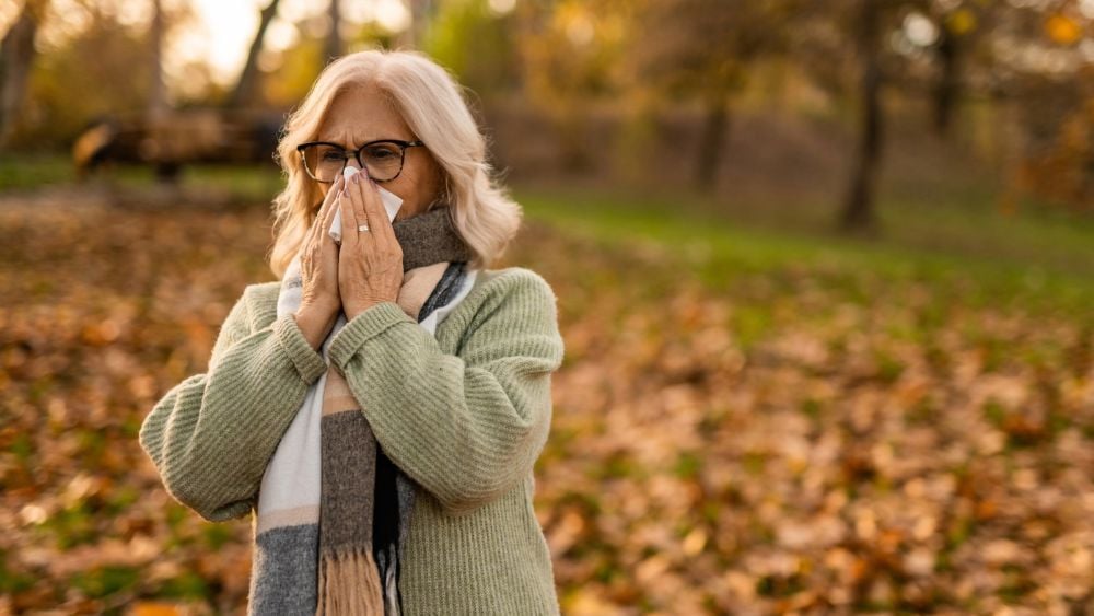 Woman blowing nose while outside in autumn weather