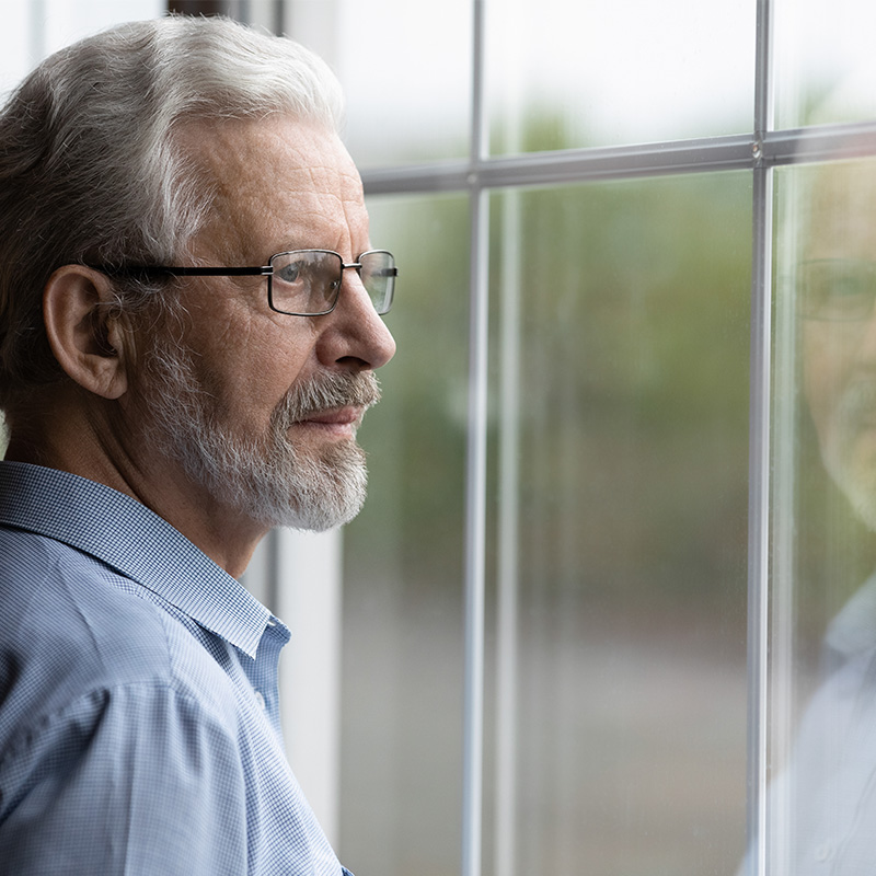 Pensive elderly mature senior man in eyeglasses looking in distance out of window, thinking of personal problems. Lost in thoughts elderly middle aged grandfather suffering from loneliness