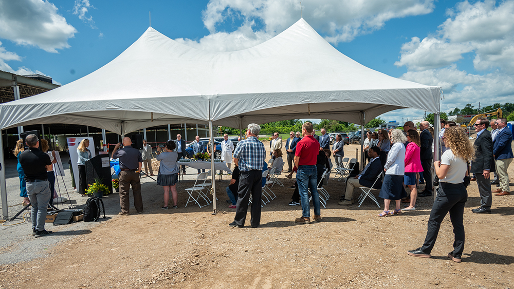 People walking around and under a white tent at a groundbreaking ceremony