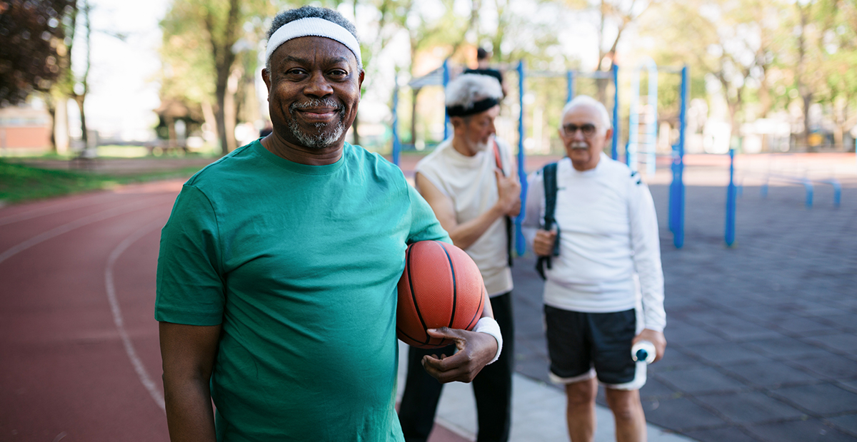 Middle aged Black man holding basketball under arm next to two other adults outside