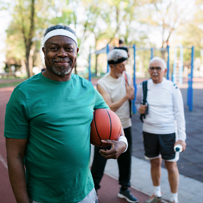 Middle aged Black man holding basketball under arm next to two other adults outside
