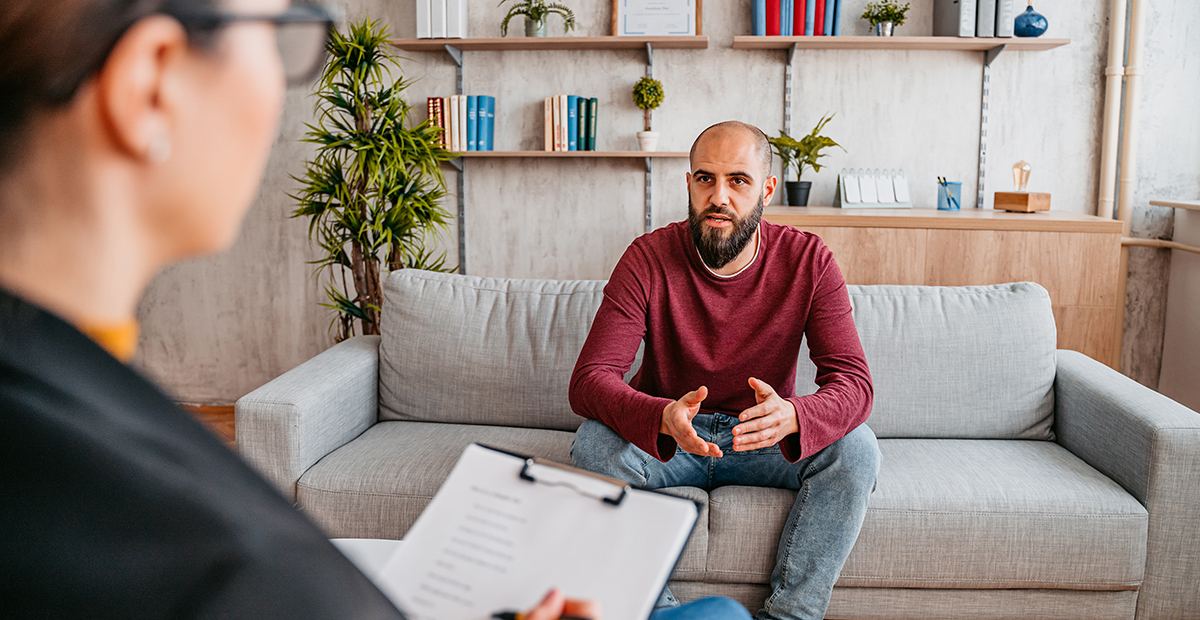 Young man with beard sits on therapist's couch and talks about his problems