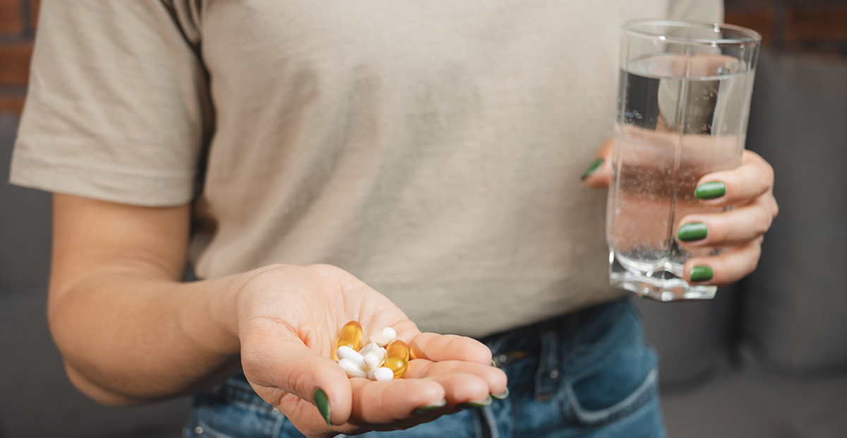 Young woman holds various medical pills and capsules in a hand and glass of water, close-up view