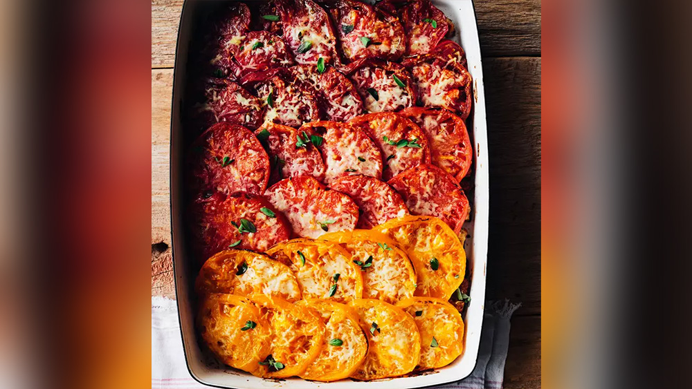 Yellow light red and dark red tomatoes artfully layered in nine by thirteen pan with herbs and cheese on top