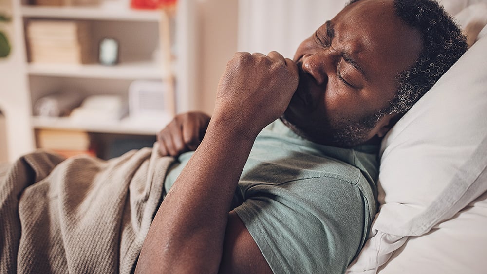Middle aged Black man coughing while lying in bed