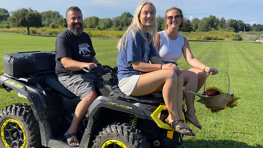 Middle aged white male on ATV with two young adult white females all smiling