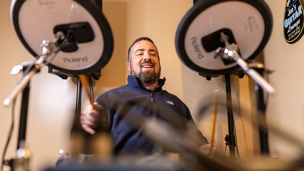 Middle aged white male smiling while playing electric drums