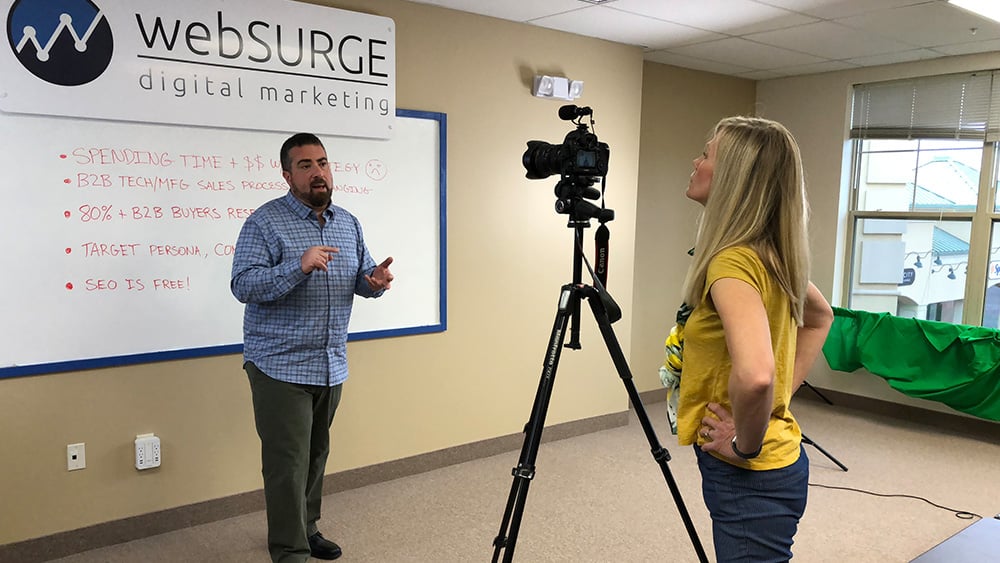White man in blue shirt talking to camera run by white woman in yellow shirt
