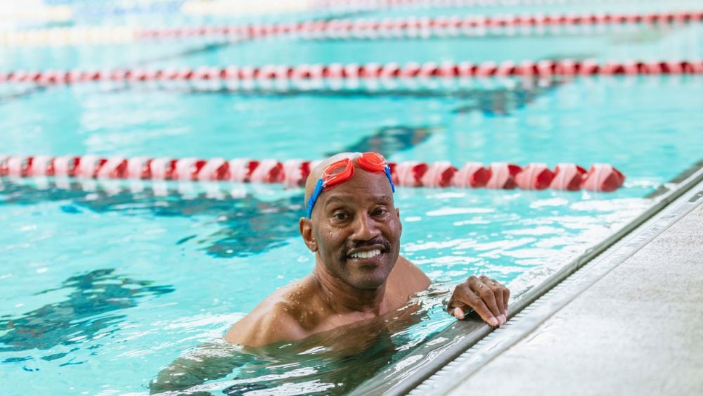 Senior African American male in 60s swimming indoors smiling at camera