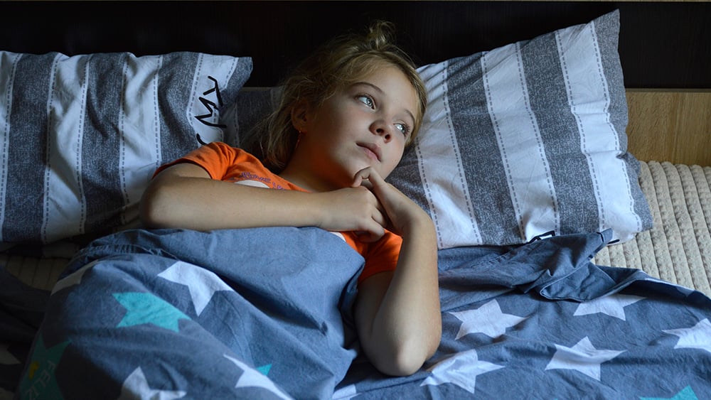 White child lying in bed awake looking out window