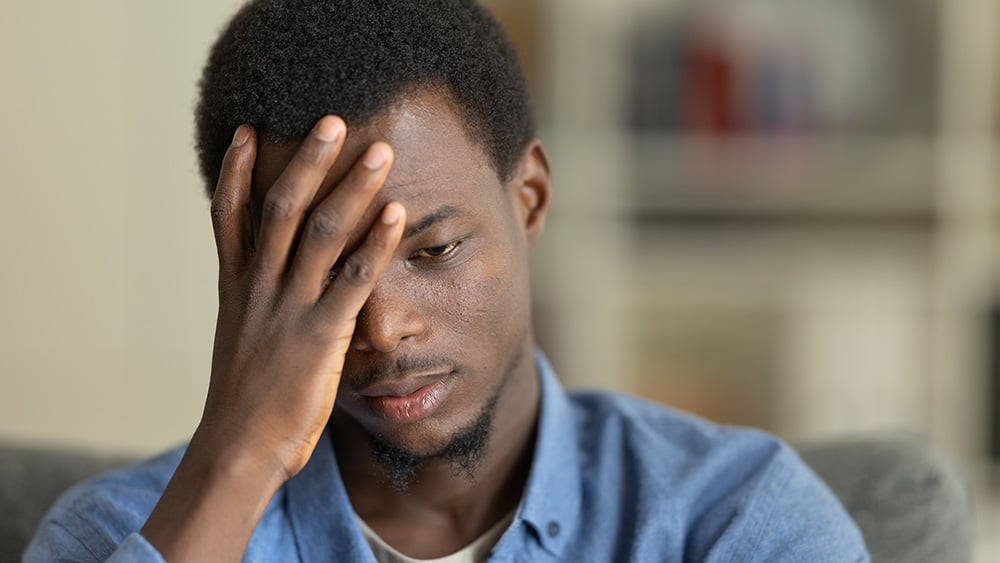Stressed young man having headache, touching his forehead, suffering from migraine or depression