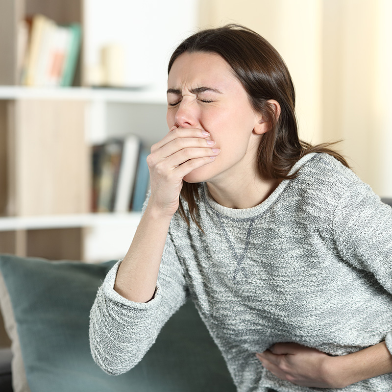 Stressed woman with a stomach ache about to vomit on a couch at home