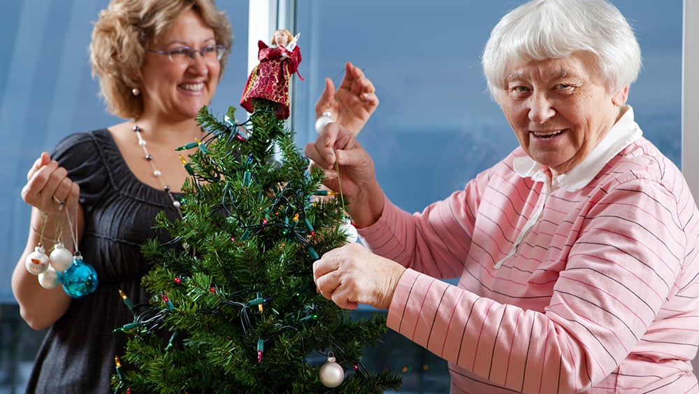 Middle aged white woman and older white woman decorating Christmas tree in nursing home