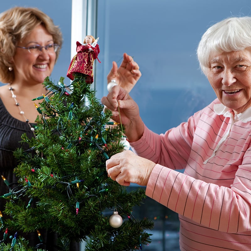 Middle aged white woman and older white woman decorating Christmas tree in nursing home
