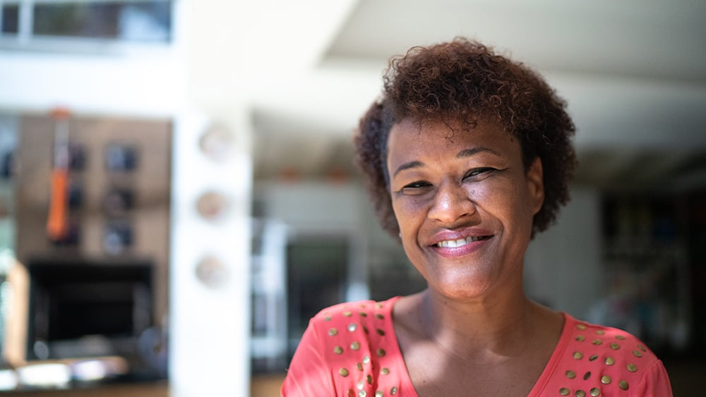 Middle aged Black woman in salmon shirt with gold sequins smiling at camera