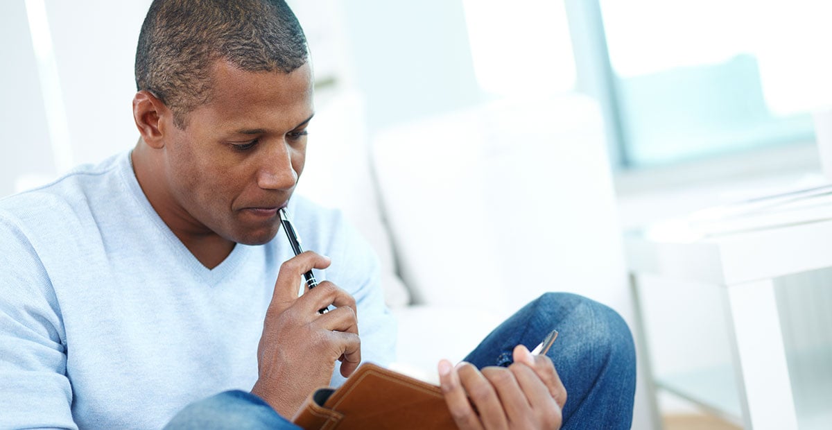 Image of pensive Black man with notepad and pen