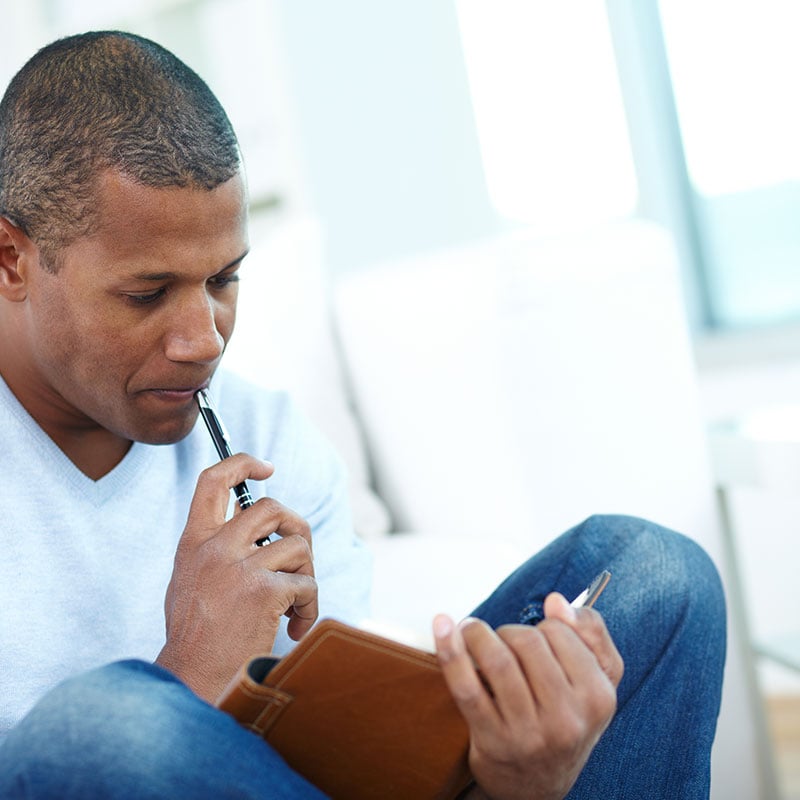 Image of pensive Black man with notepad and pen