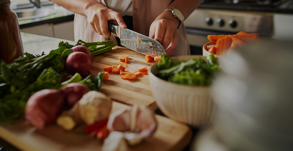 Closeup of young female hands chopping fresh vegetables on chopping board while in modern kitchen