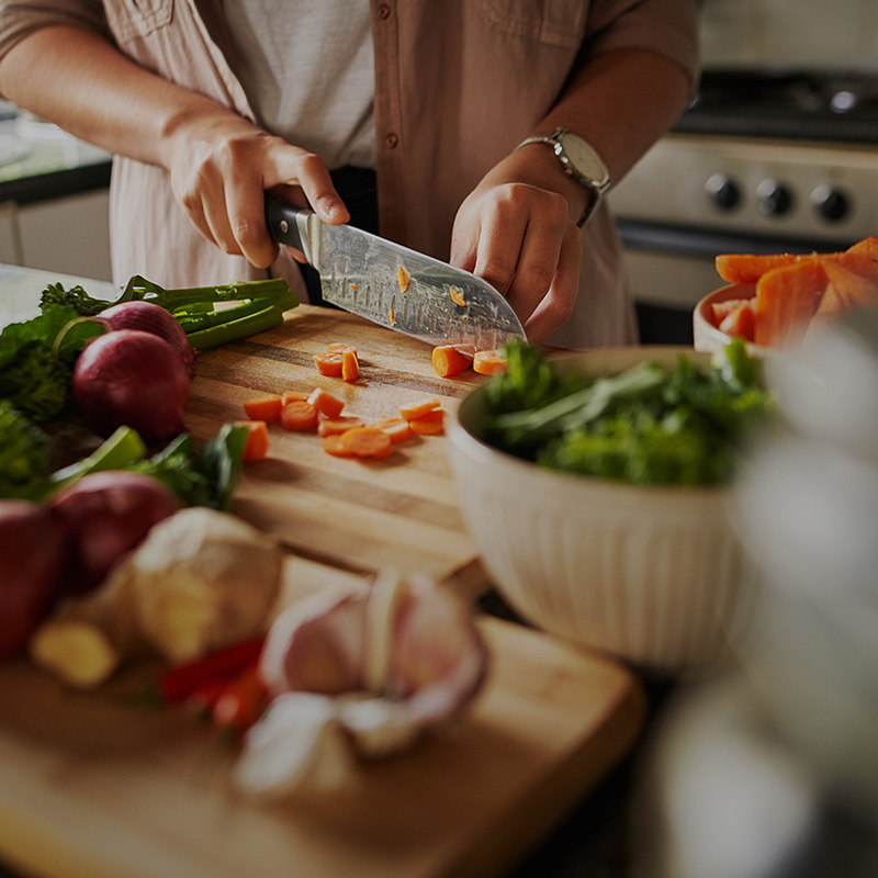 Closeup of young female hands chopping fresh vegetables on chopping board while in modern kitchen