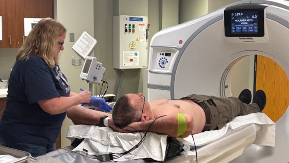 White female medical professional helps shirtless white male in imaging scanner